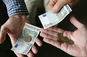 Real-term wages are falling. Image relates to minimum wage with hands holding low denomination euro notes and coins.