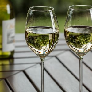 two wine glasses containing white wine and a bottle