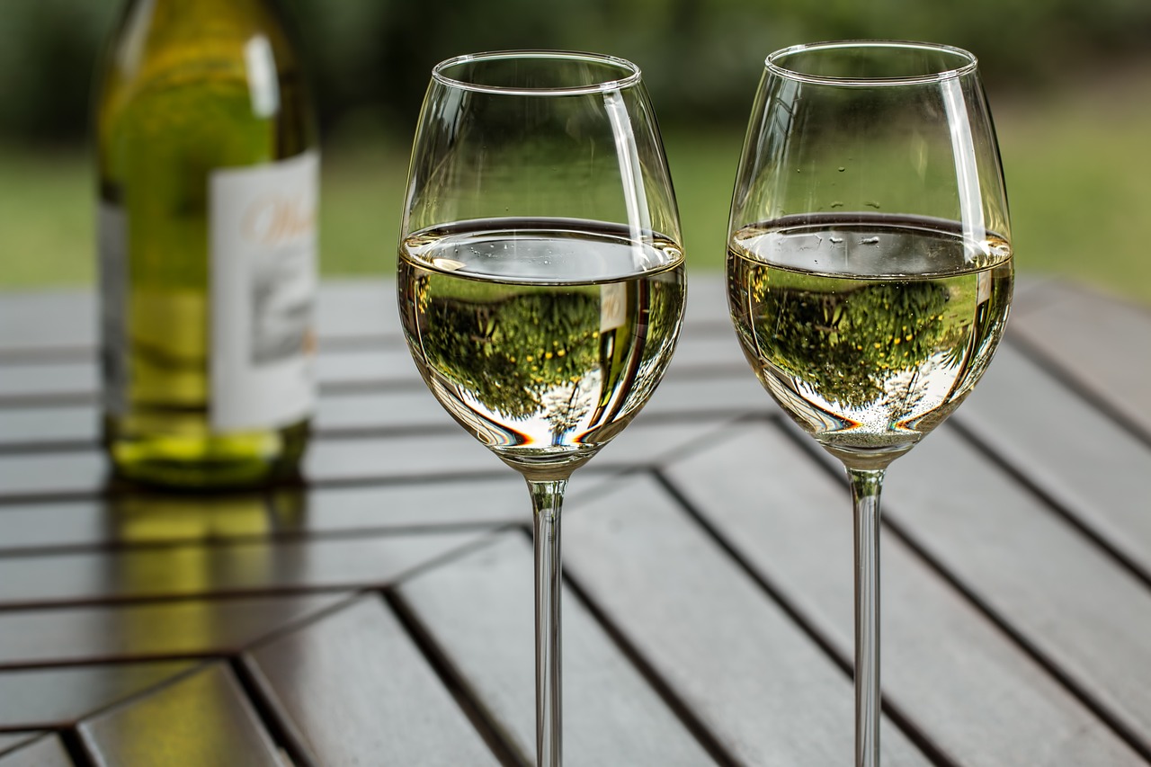 two wine glasses containing white wine and a bottle