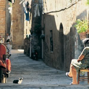 Retirement aage in pension could be as higha s 71 for young Italians. Image shows older lady sitting on chair in Italian back street.