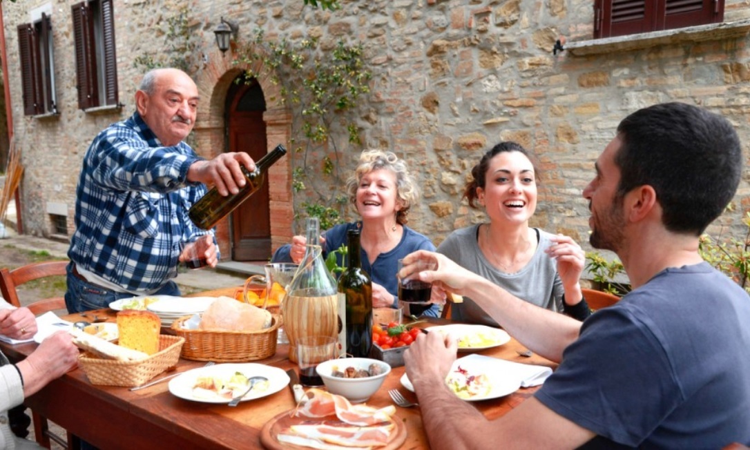 Italian cuisine is a way of connecting with family. Image shows family eating outdoors as the older man offers red wine