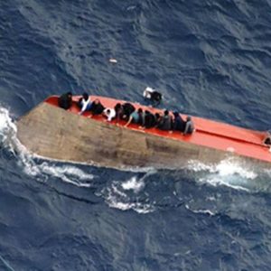 Migrants cling to upturned boat as merchant vessel approaches to rescue them. Image credit Sea Watch on X