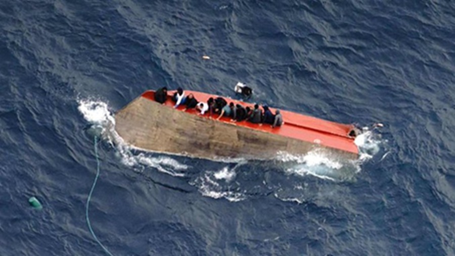 Migrants cling to upturned boat as merchant vessel approaches to rescue them. Image credit Sea Watch on X